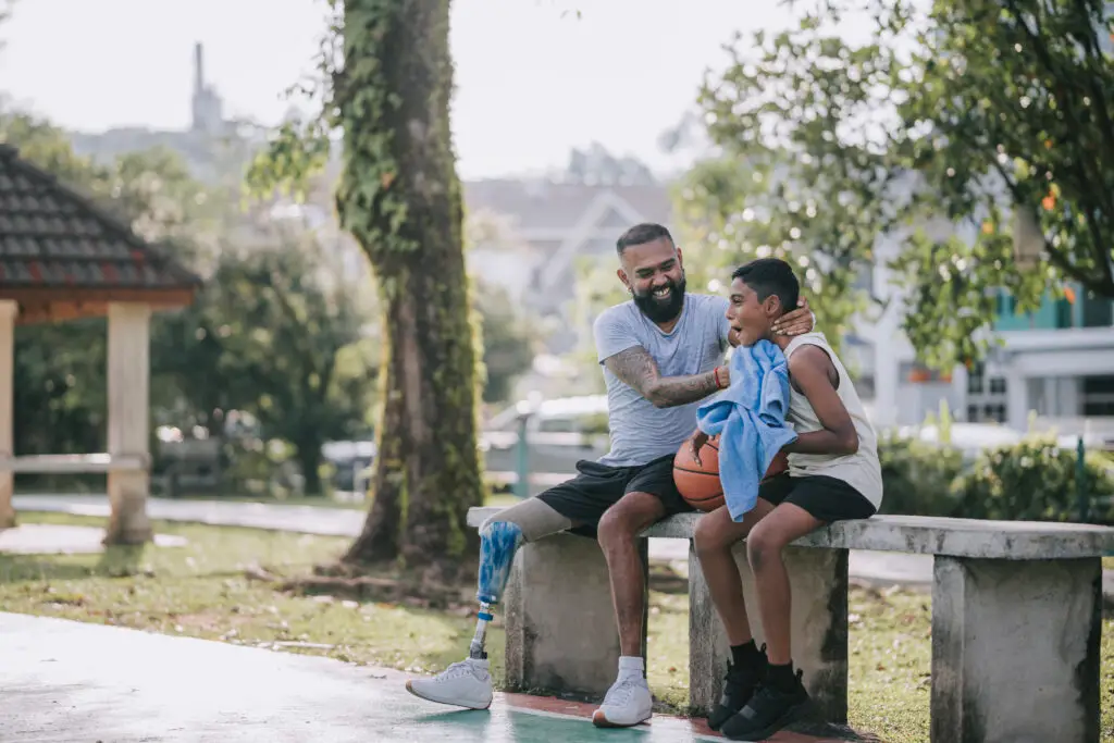 Asian Indian father with disability helping son wiping sweat with towel after basketball game